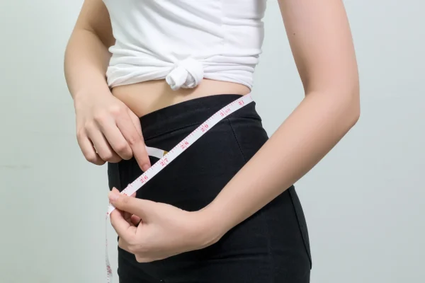 midsection-young-woman-standing-against-white-wall